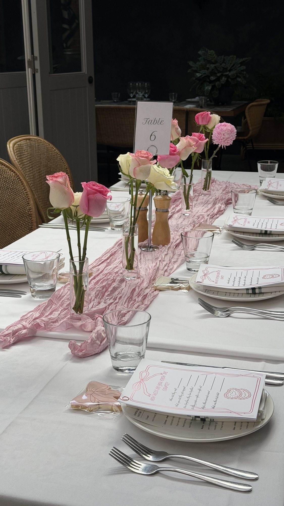 Single pink rose stems in bud vases along a white table with a blush runner