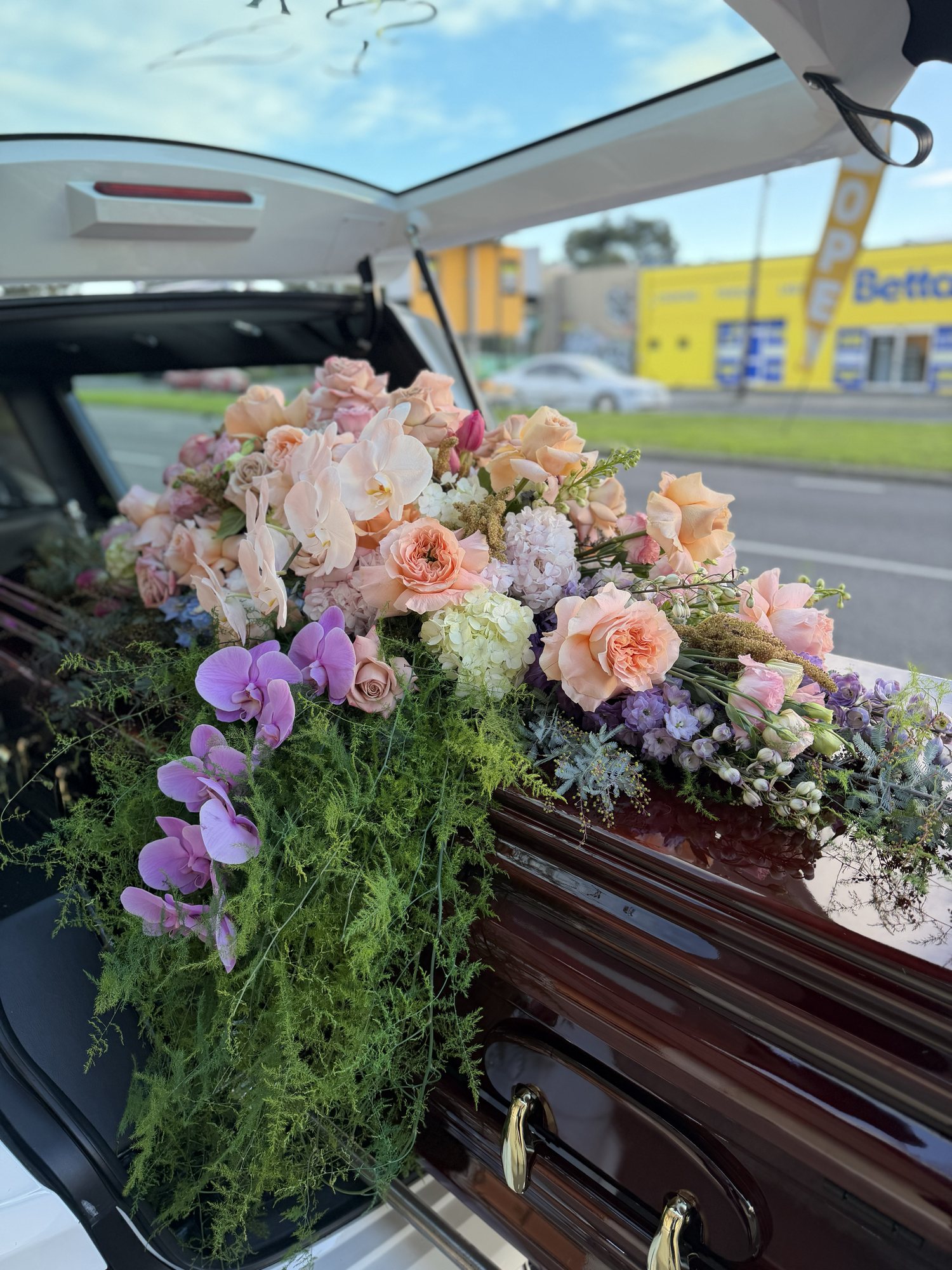 Custom casket spray of peach roses, purple orchids and trailing greenery
