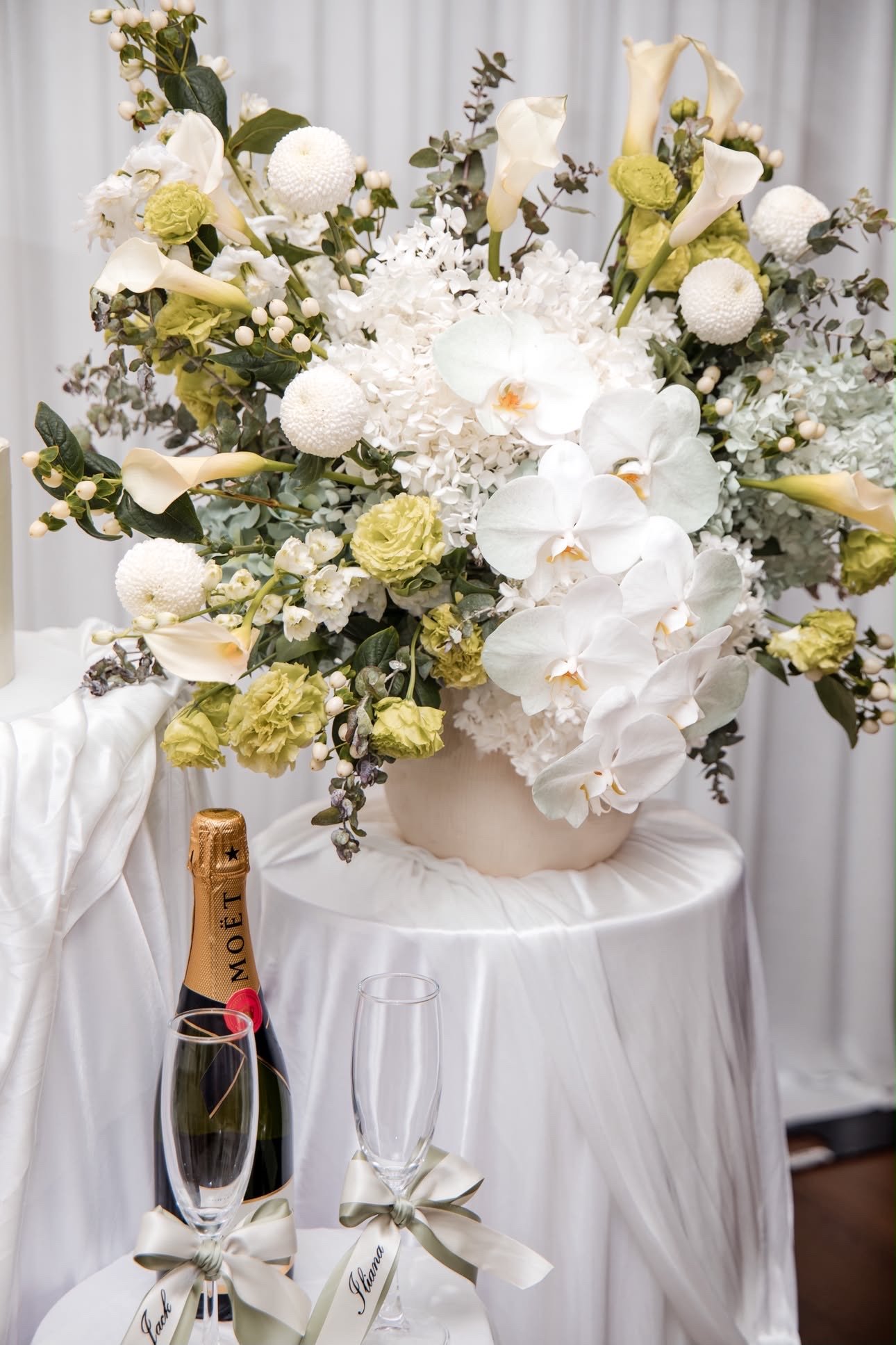 White orchid, rose and calla lily arrangement in a vase with champagne and flutes