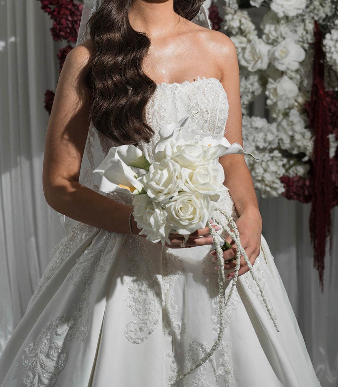 Bride holding a white calla lily and rose bouquet in front of a floral wall