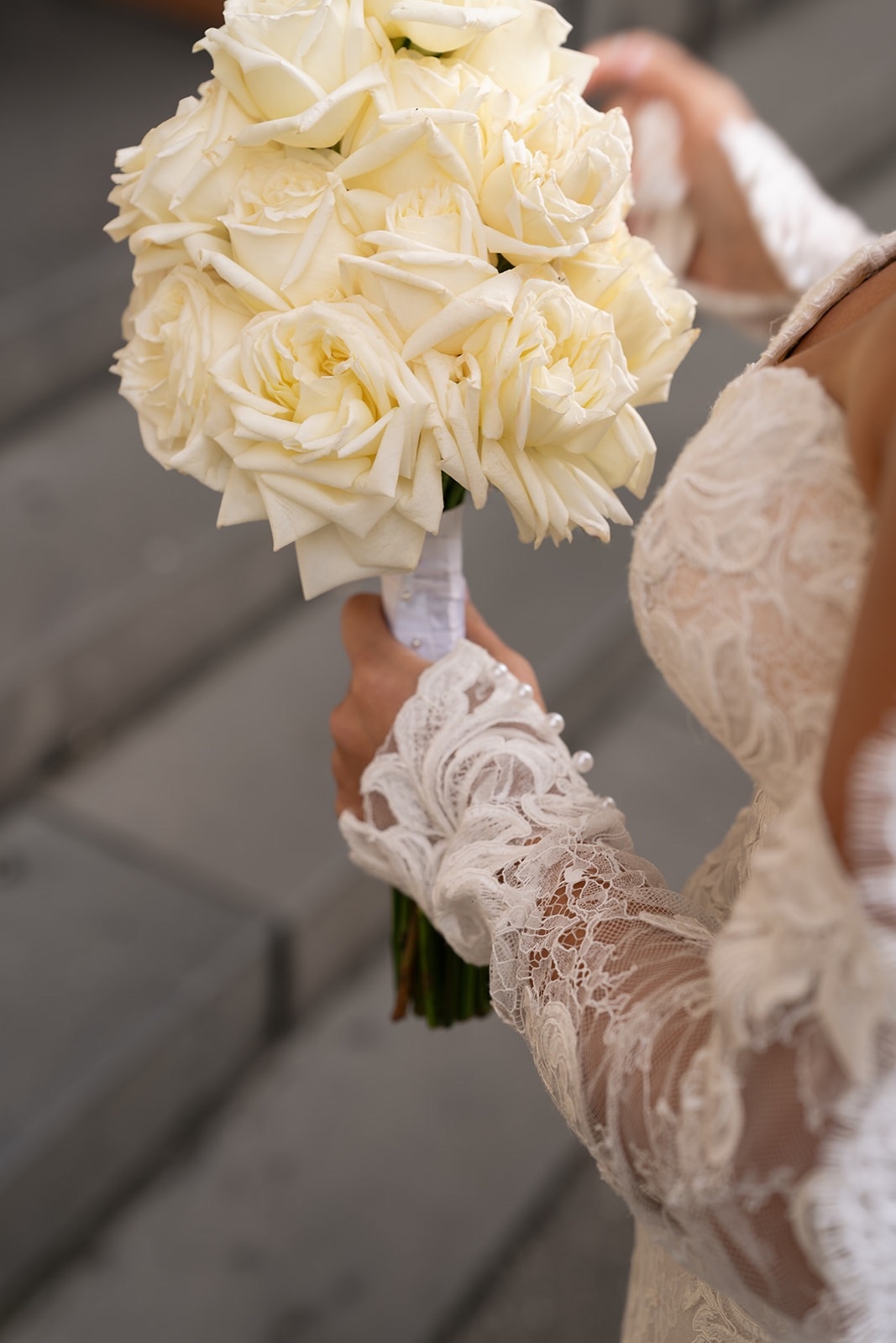 Ivory rose bouquet detail, bride's lace sleeve visible